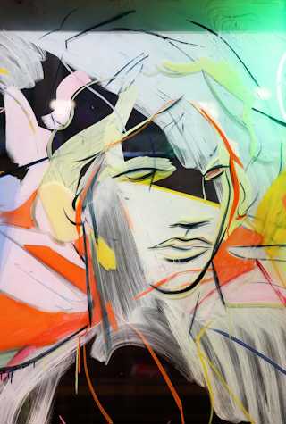 Close up of a painting on glass depicting a face with black fast strokes and blocks of pale blue, pink, green and orange through