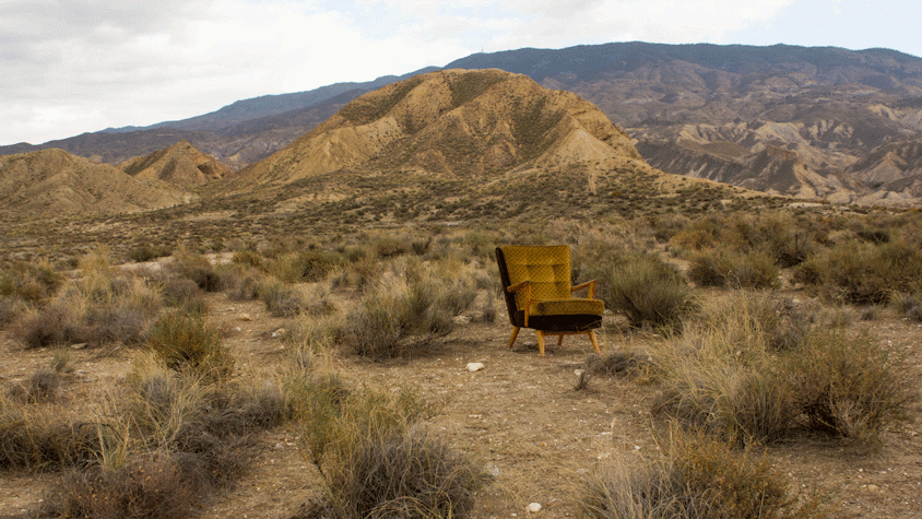 A film still showing a rocky landscape with an arm chair