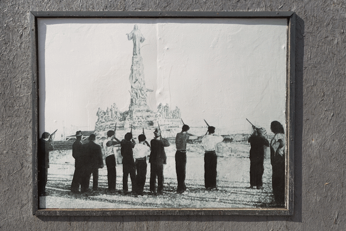 a billboard displays an intricate pencil drawing of a group of people pointing rifles at a statue