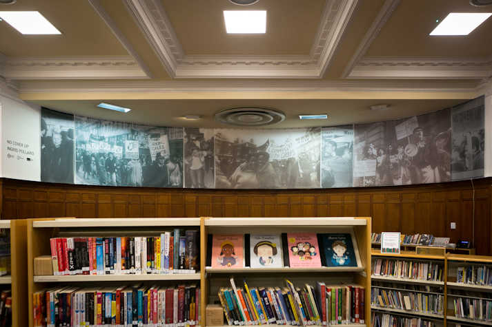 Interior of Glasgow Women's Library showing bookshelves in the foreground, and archive imagery (black and white photos) in the backgorund