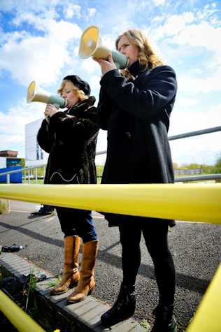 two women speaking into megaphones standing outside behind a yellow barrier