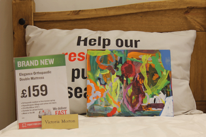 Colorful abstract painting laid in some cushions in a British Heart Foundation charity shop.