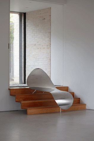 There are some small wooden stairs leading to a window. On top of that there is a sculpture made of silver metal that looks like an ondulated chair.