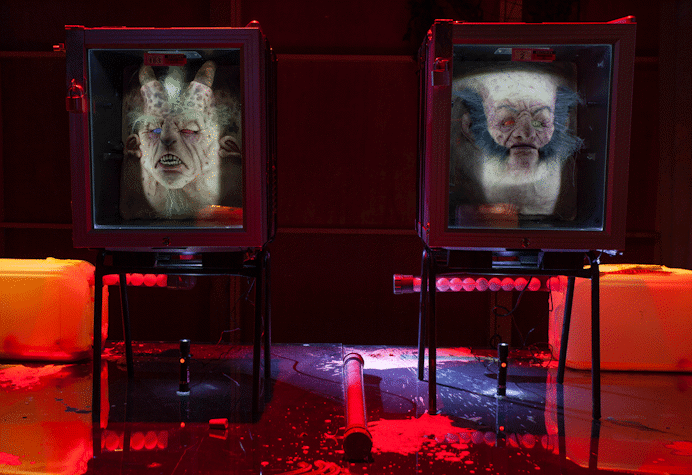 An image of jenkin van zyl's installation. There are 2 fridges holding mangled heads, panels from an aeroplane and eerie red lighting.