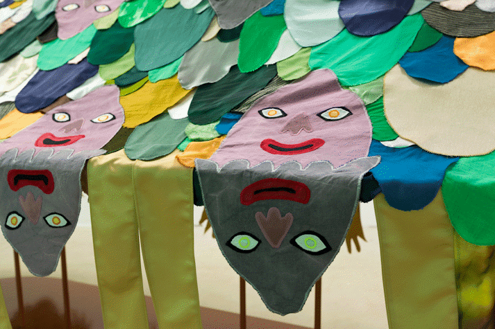 image of a large scale surreal sculpture with 5 baby-like heads, wiggling arms and a patchwork of fabric cut outs laid over it in the shape of cartoon-like arms and faces