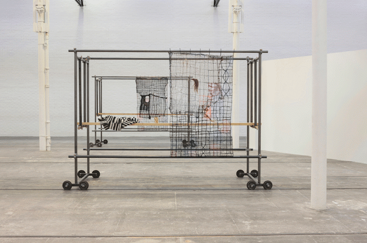 Two trolleys have dark pieces of fabric hanging from it. White room with white columns and grey floors.