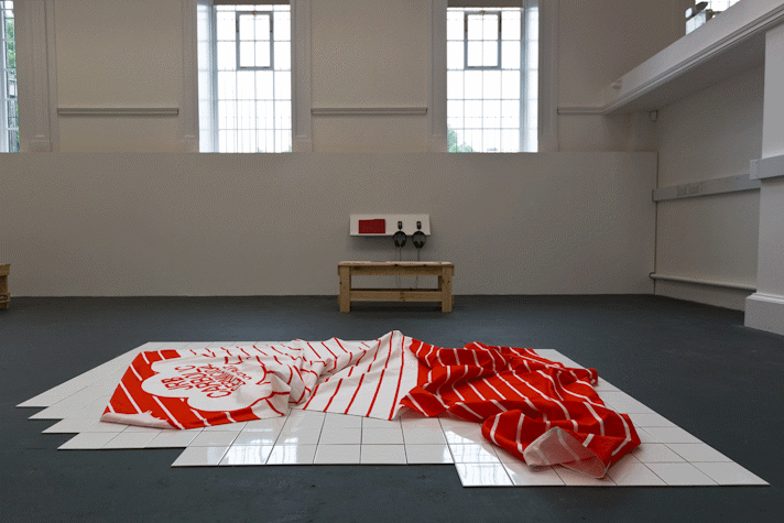 a red and white piece of striped fabric with printed lettering lost in folds sits on a section of white tiled floor
