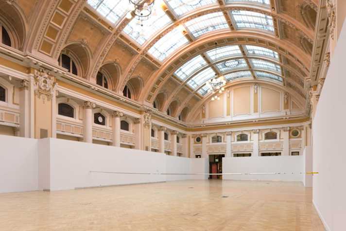 sculptural installation of chrome-coated pipe stretching across a large victorian hall