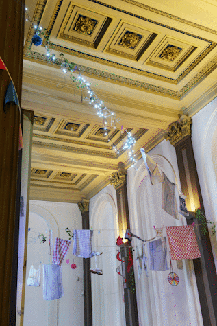 Elegant barroque-decorated ceiling and columns with colorful laundry hanging across the room as part of an art installation in the Gallery of Modern Art, Glasgow International 2018.