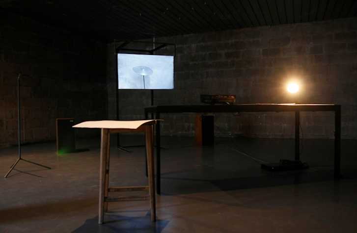 dark room with a wooden table and stool. in the background there is a small tv monitor
