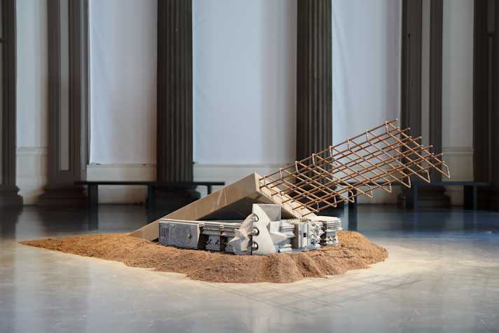 An image of Nirbhai (Nep) Singh Sidhu's installation in the Gallery of Modern Art, Glasgow. The image show an abstract sculpture made of concrete and steel laid on a pile of sand.