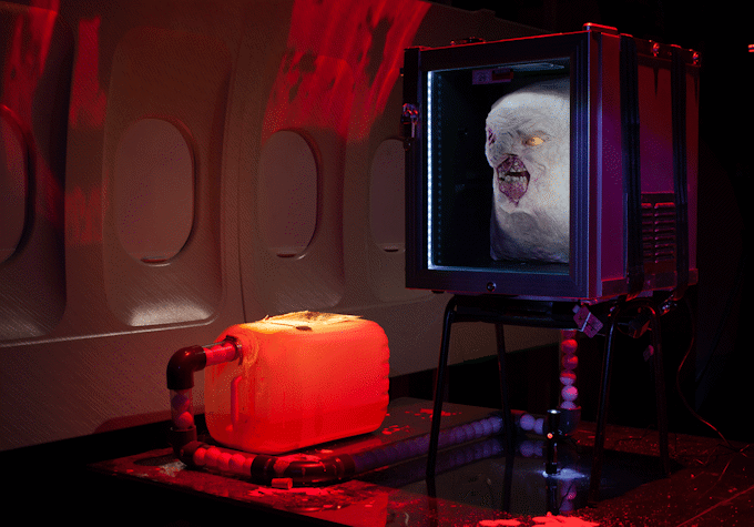 Image of Jenkin van Zyl's installation at Tramway. The room sits in eerie red light with strange panels of an aeroplane, a watertank, pipework and fridge.