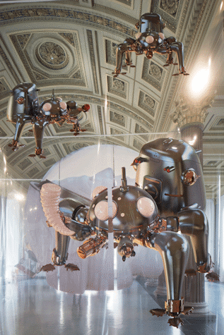 Three large mechanical looking insects are printed on polyester foil panels, they seem to be suspended from the ceiling. They have 4 legs and big, pink, bulbous eyes. The carry big container looking shells on their backs. Their mouth and feet are bronze while their bodies are silver.