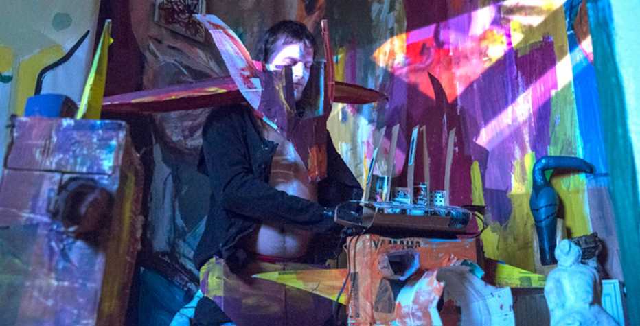 Photograph of a performance with figure in a cardboard and coloured paper installation