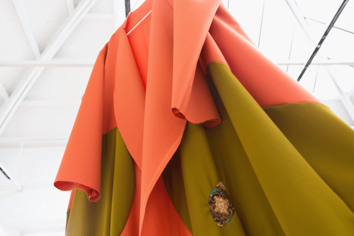 detail of a large fabric cape in orange and kahki that is suspended from a high ceiling
