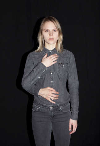 woman stood with one hand on her chest and the other at her side. another arm reaches from behind her and rests their hand on the woman's stomach.