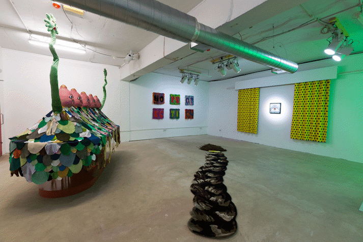 installation view of exhibition with a large scale surreal sculpture, a floor work mimicking a rug and depicting an oversized braid, 6 carpet wall works, a small painting with patterned curtains hanging either side
