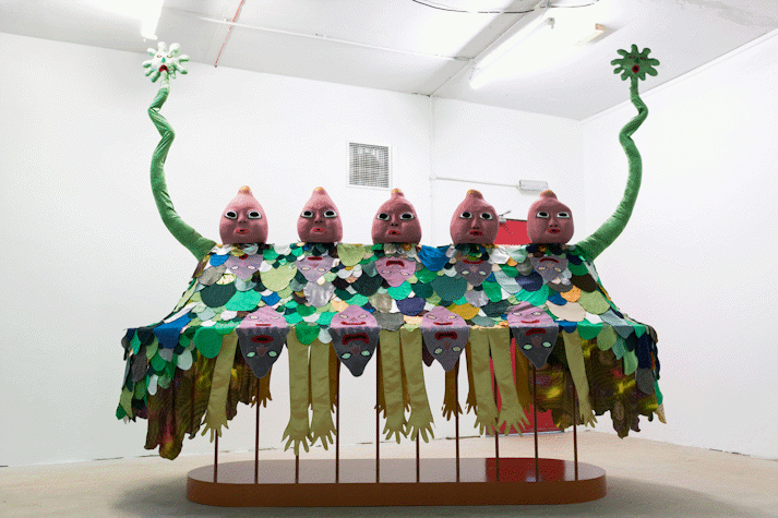 image of a large scale surreal sculpture with 5 baby-like heads, wiggling arms and a patchwork of fabric cut outs laid over it in the shape of cartoon-like arms and faces