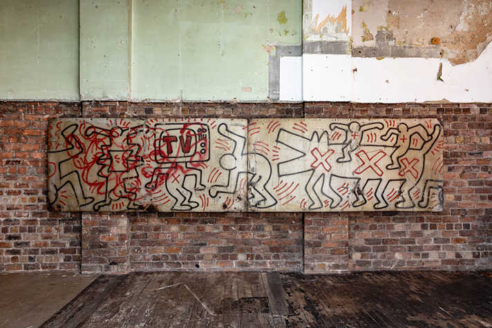 A long illustrated artwork is displayed on a brick wall.