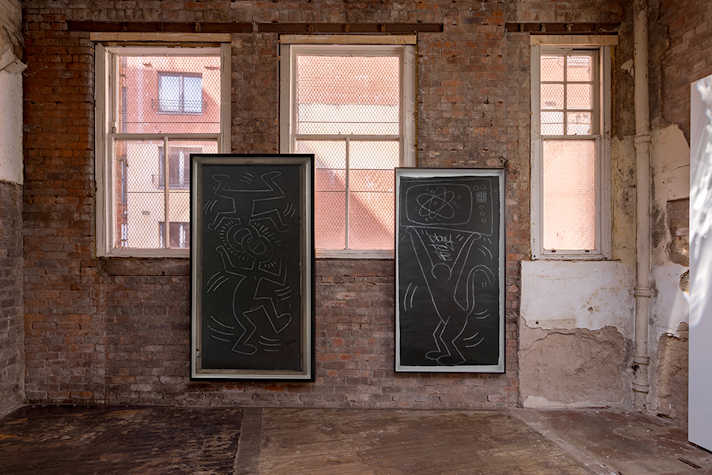 Two large artworks are displayed on a brick wall next to two large windows.