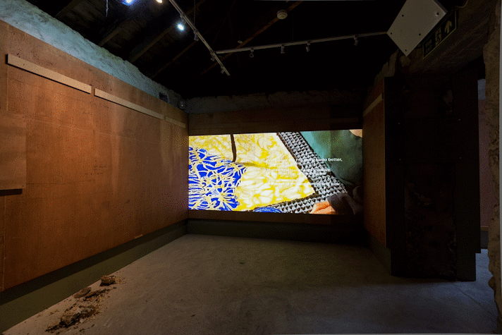 a projected film shows a brush stroking ink over calico and a wax pattern