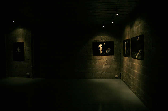 dimly lit room with brick walls. there are four works on the walls lit from above.