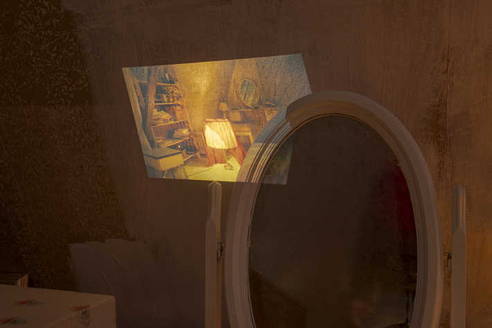 In a dimly lit room, there is a projection onto a wall, overlapping onto an oval mirror.