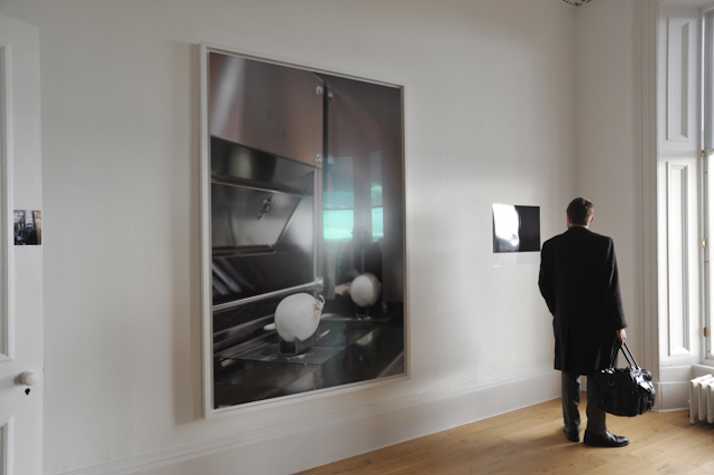 large framed image of an onion on a cooker. a man dressed in all black looks at a smaller photograph next to it.