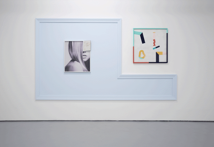 There is a large frame covering the space on the side of and around a square multimedia artwork. There is a small framed photograph placed in its centre.