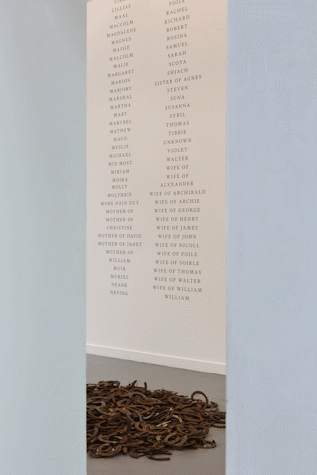 a pile of horseshoes on a grey floor. in the background is white wall with columns of black text listing surnames