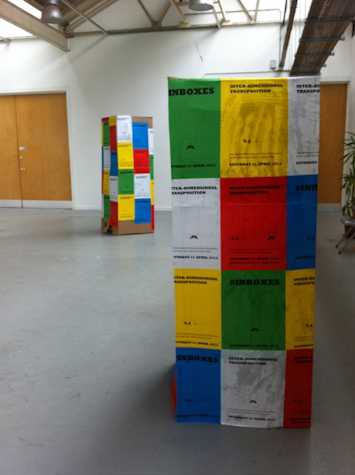 two tall cardboard boxes with red, white, yellow, blue and green posters pasted onto them.