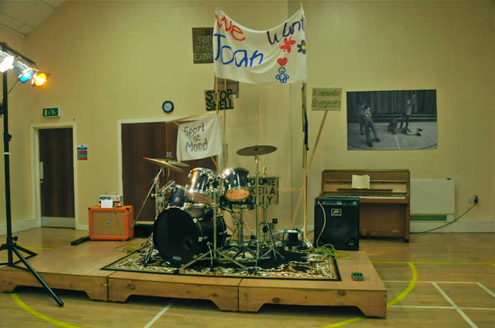 A drum kit in a village hall with a banner behind it