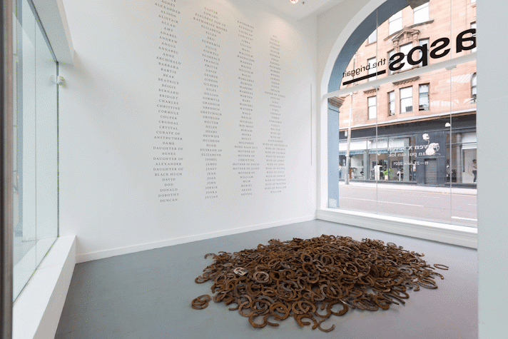 a pile of horseshoes on a grey floor. in the background is white wall with columns of black text listing surnames