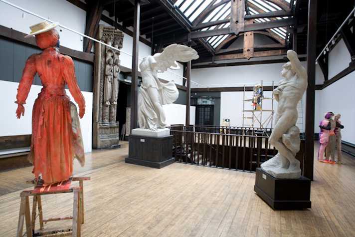 room with painted orange statue in foreground and two white marble statues in background