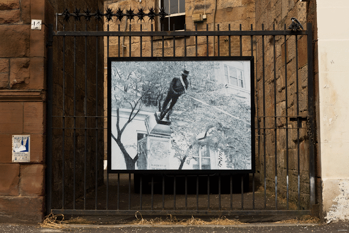 a billboard displays an intricate pencil drawing of a statue being toppled