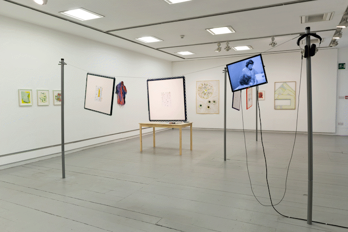 paintings hang on the walls of a gallery. in the middle of the space a wire hangs between two washing line poles, two artworks and a small tv monitor hang from the wire