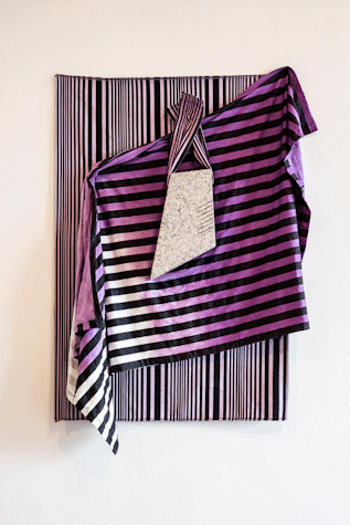In front of a panel of black and white stripped cloth with vertical lines there is a cloth of black and purple to white gradient lines that go horizontally, these are thicker than the background vertical lines. In front of the cloth there is a piece of grey rock that is smoothed into an uneven quadrilateral. It is held by a string-like cloth with black and white horizontal lines stapled to the canvas. This is part of an art installation in Tramway as part of Glasgow International 2018.