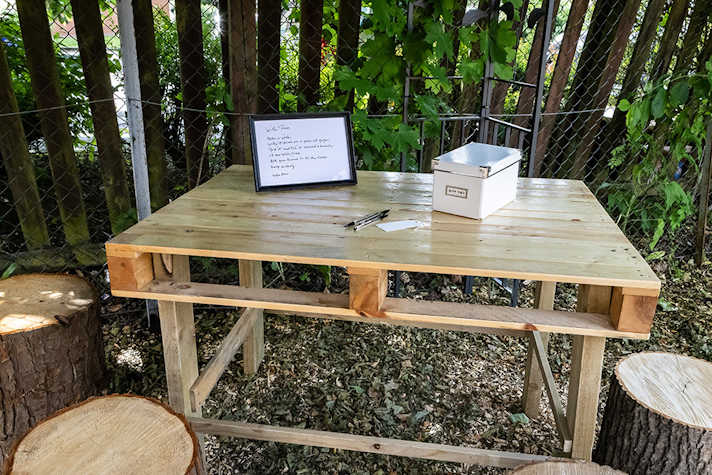 A framed messages and a box sit on top of a wooden table in an outdoor area.
