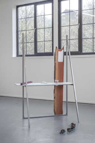 Sculptural work with metal frame, shelf and wooden plank in a gallery with a window behind