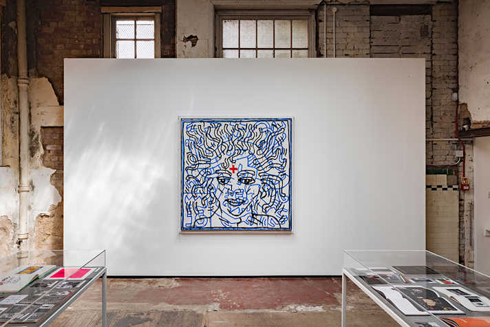 A white and blue square artwork is displayed on a white wall, in an industrial space.