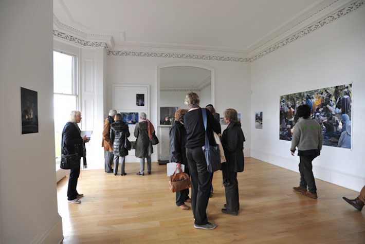 large bright room with spectators looking at photographs hung on the walls.