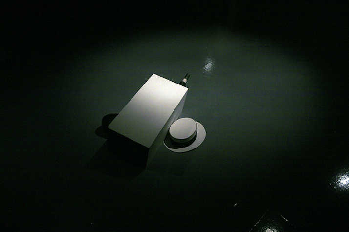 there is a white box on the floor with a white Panama hat next to it. a small black tube pokes out the white box.
