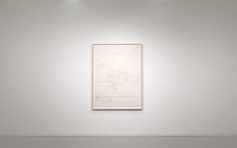 a pencil drawing of an aerial view of a landscape hangs, framed, on the white wall of a gallery