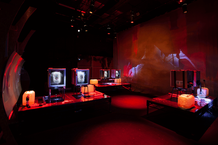 An image of jenkin van zyl's installation. There are 3 fridges holding mangled heads, panels from an aeroplane and eerie red lighting.