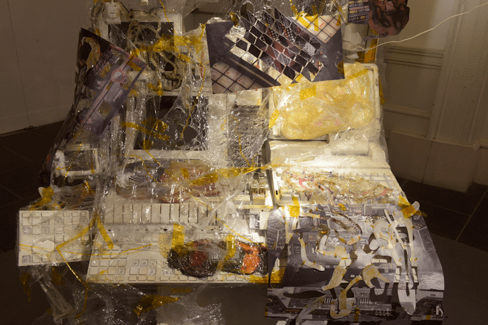 A desk with a computer and a keyboard covered in newspapers and other plastic textures as part of an art installation in the Gallery of Modern Art, Glasgow International 2018.