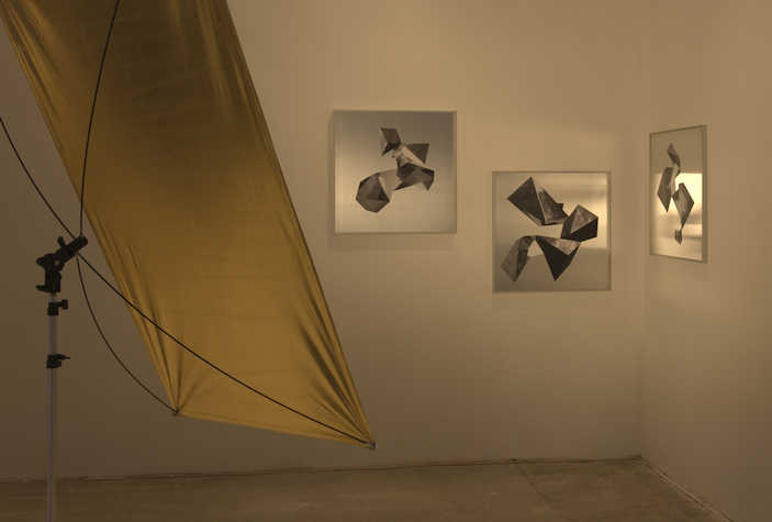 three geometric illustrations on mirrors hung on a wall. in front is a large metallic reflector.