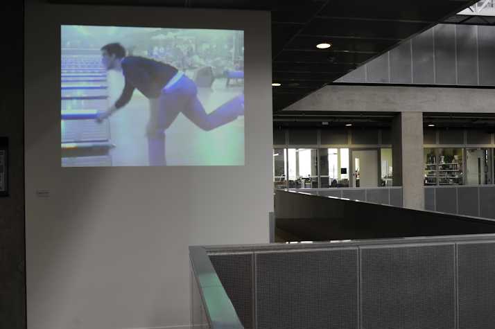 film projected in an office atrium space. the projection shows someone mid bowling
