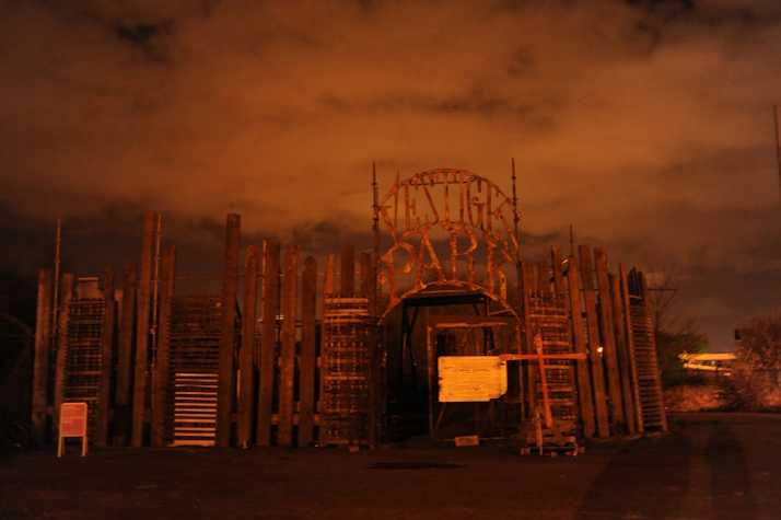 orange filtered image of a large wooden fence. atop is a sign reading 'vestiges park'