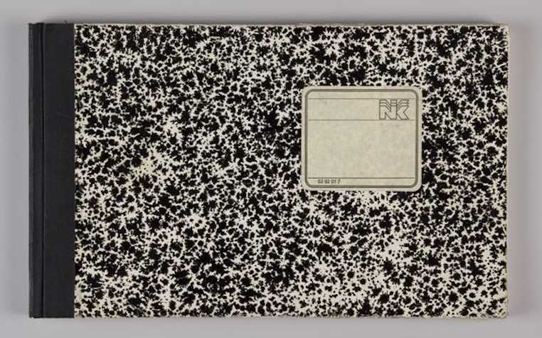 landscape composition book with black tape binding and a black and white dappled cover. there is an off white square label with a logo 'NK' and the numbers '52 91 01 7'