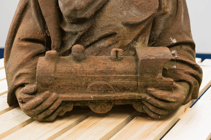 detail of a red sandstone sculpture showing hands holding a small train